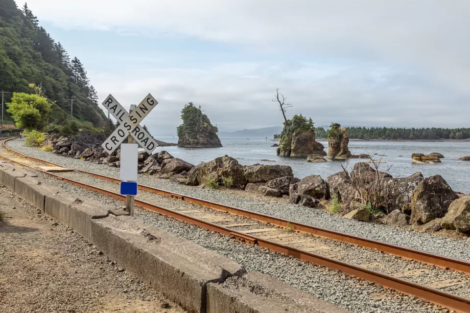 Railroad crossing sign next to tracks along rocky coast in Oregon.